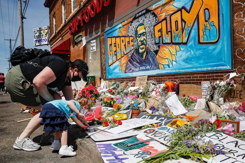 A woman and child place flowers along a memorial wall for George Floyd.