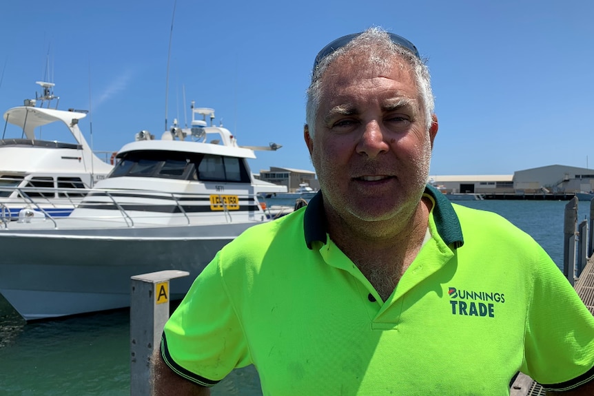 Portrait shot of Justin Pirrottina wearing fluro yellow shirt in front of a boat at Geraldton Fishermen's Wharf.