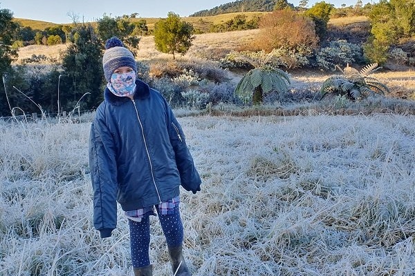 Person rugged up standing in a frosty paddock.