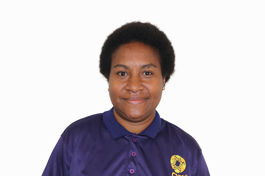 Woman wearing purple shirt with CARE logo looks at camera smiling. Short black afro style hair and brown eyes. 