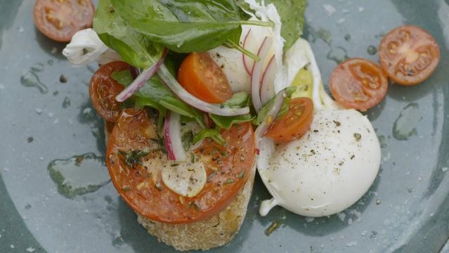 A dish of poached eggs, tomato and green leaves on toast