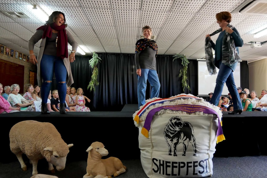 Three women on a raised catwalk modelling wool outfits.