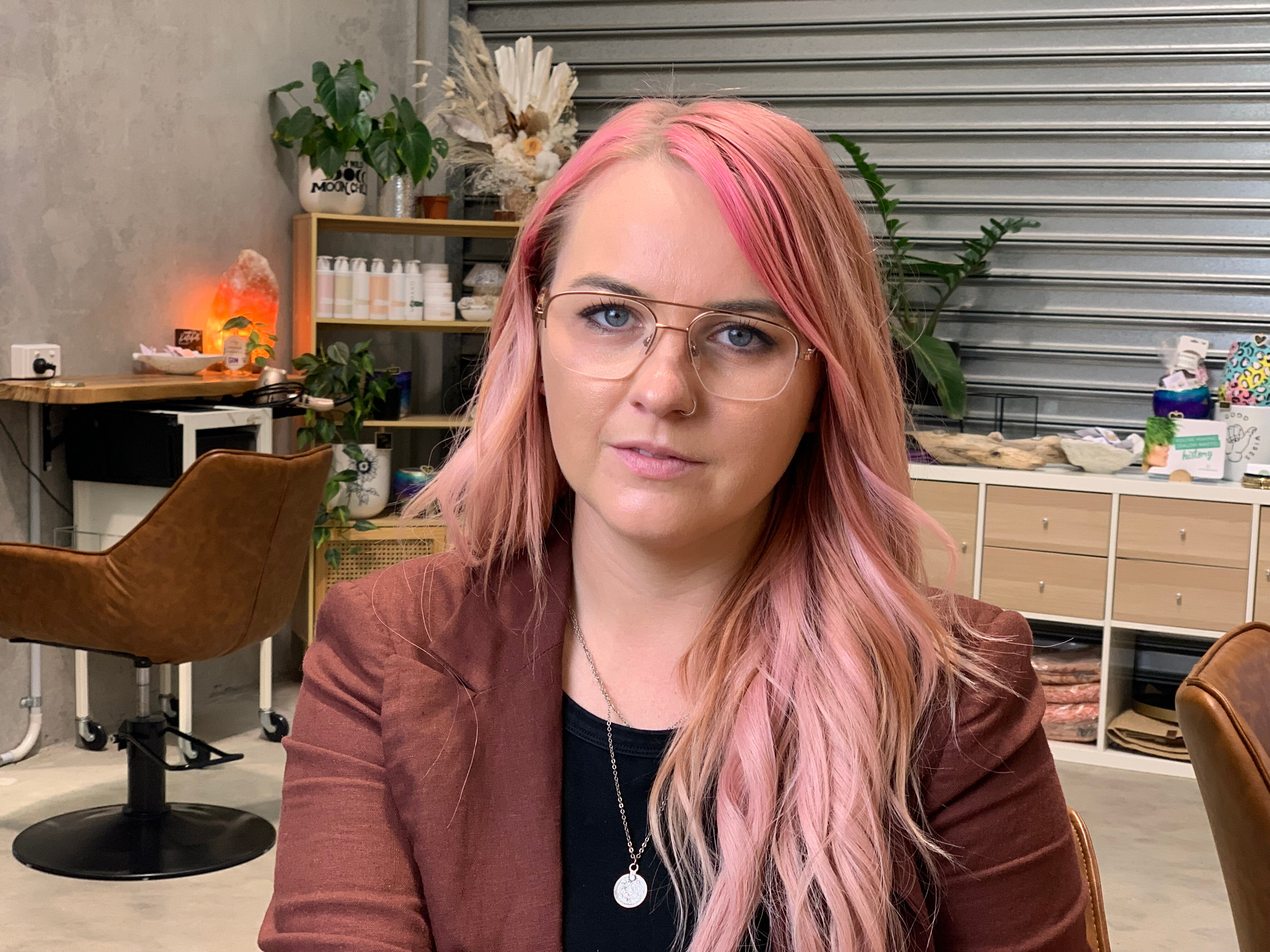 Woman sitting in a salon.  She has long, fair, hair that has been dyed pink.