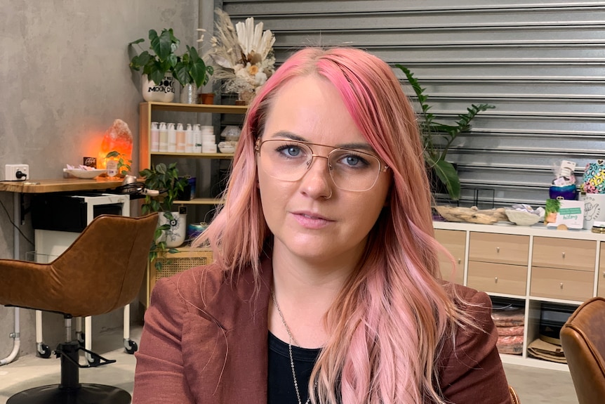 Woman sitting in a salon. She has long, fair, hair that has been dyed pink.