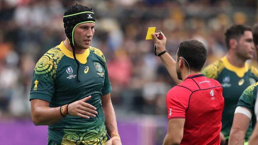 A Wallabies player wearing headgear is shown a yellow card from the referee at the Rugby World Cup.