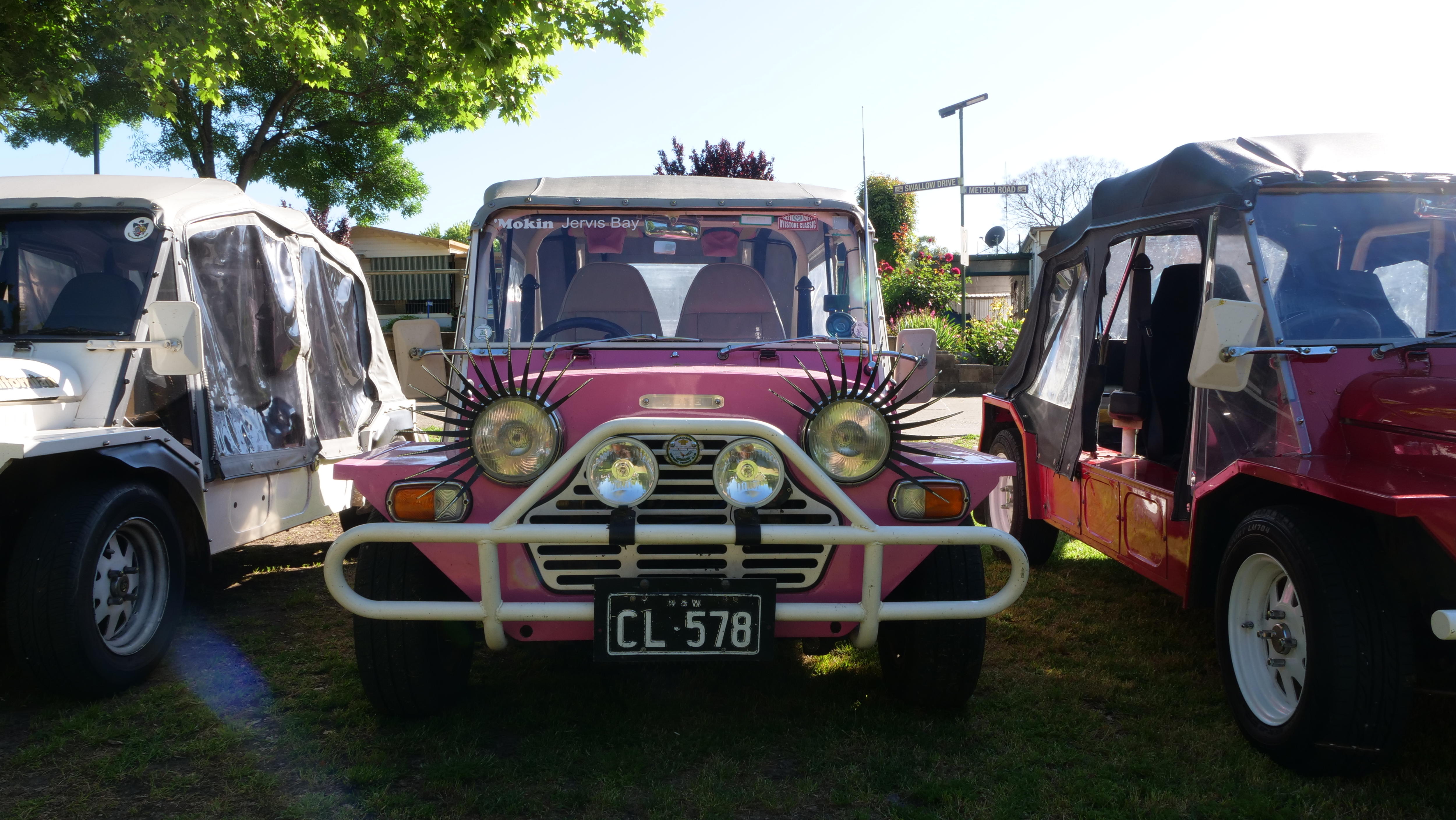 A small, pink car called a Mini Moke with eyelashes extending from the headlights.