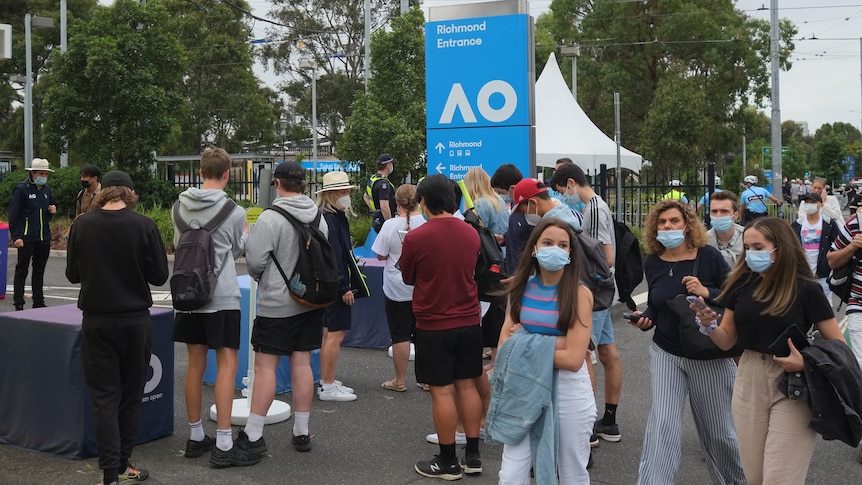 A bunch of masked men and women walk past a sign that says AO, the Richmond entrance. 