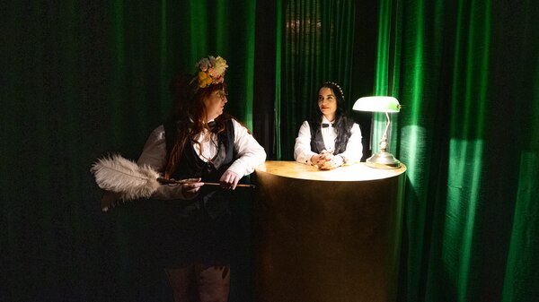 Two ladies wearing feathered and formal attire sit in a dimly lit room.