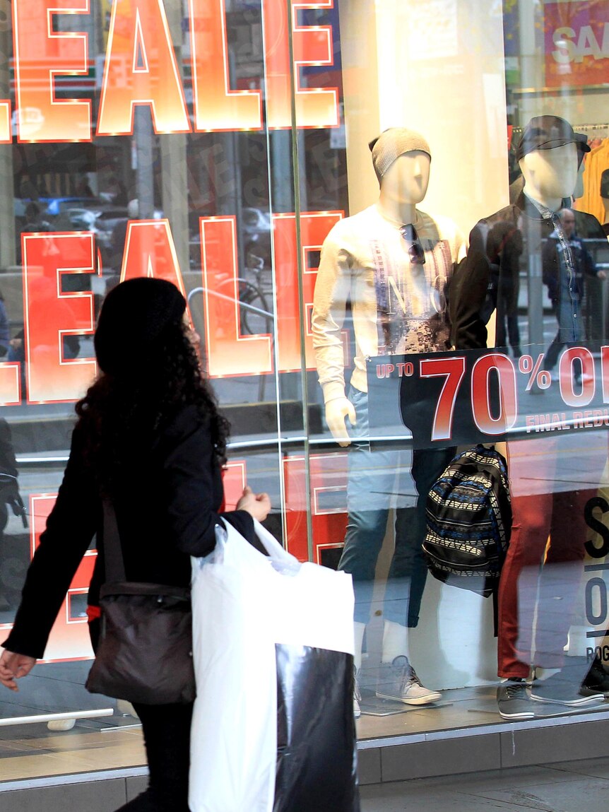 A woman walks past a store displaying sale signs.