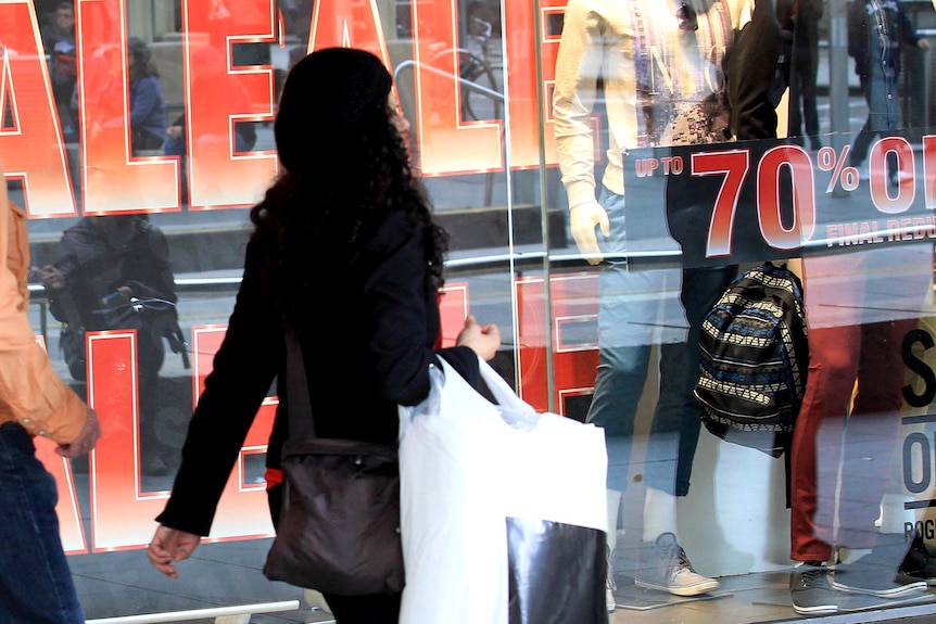 A woman walks past a store displaying sale signs.