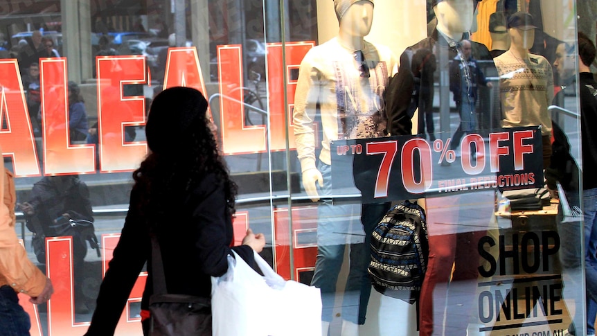 A woman walks past a store displaying sale signs.