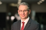 A headshot of Michael Riches, the NT anti-corruption commissioner wearing glasses and a suit with a blurred background