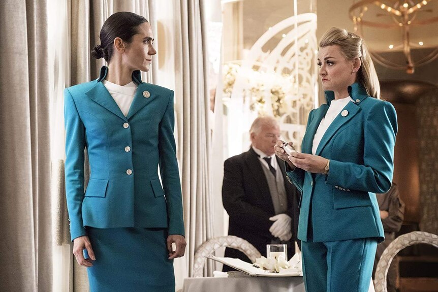 Two women in blue blazers stand in an opulent room
