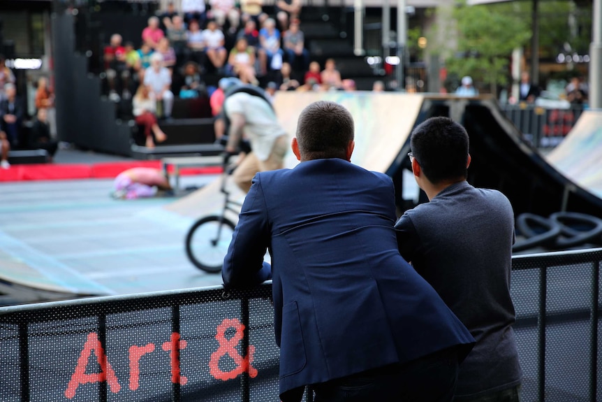 David Lawrence-Watt and Will Curtis stand facing away from the camera watching BMX riders.