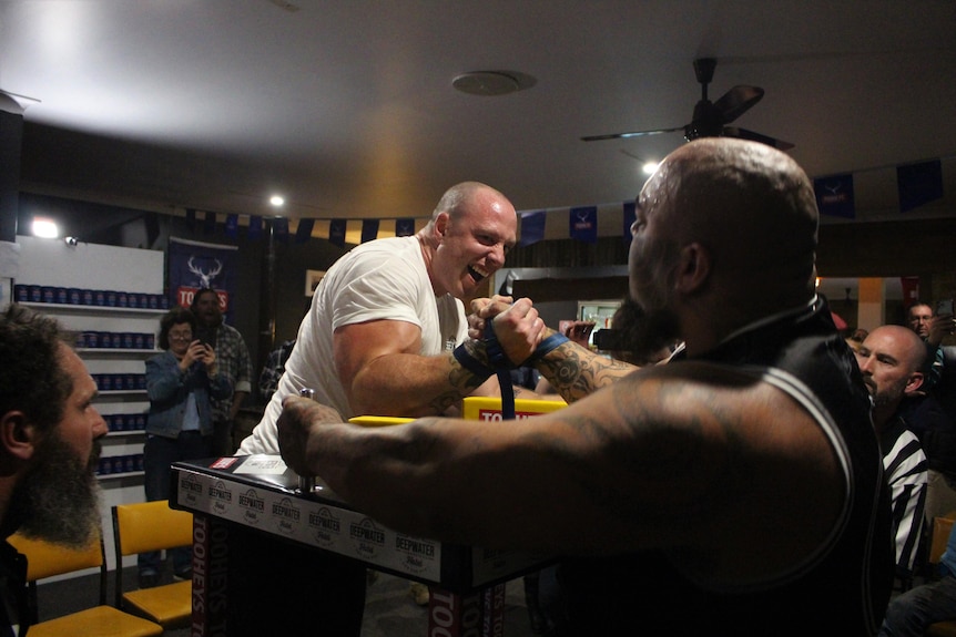 A man sticks his tongue out in expression as he arm wrestles. 