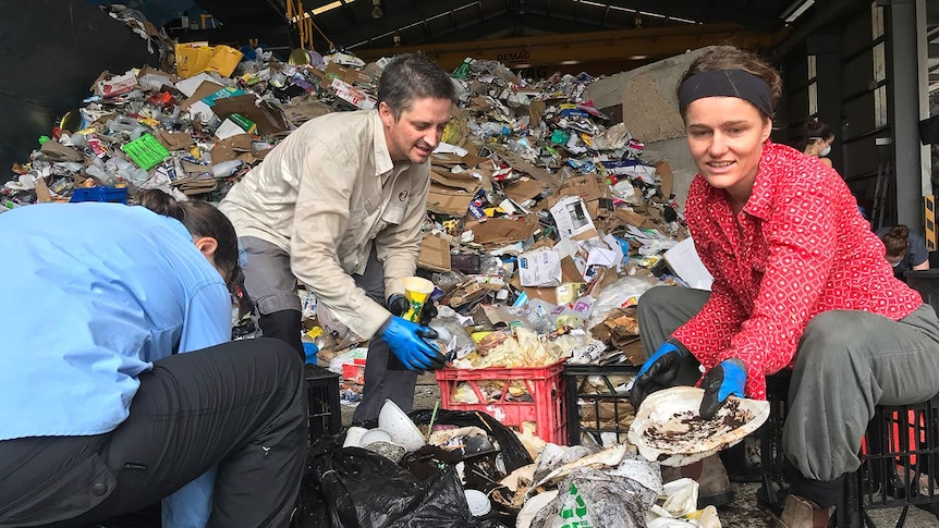 A photo of volunteers sorting through waste in an industrial shed.