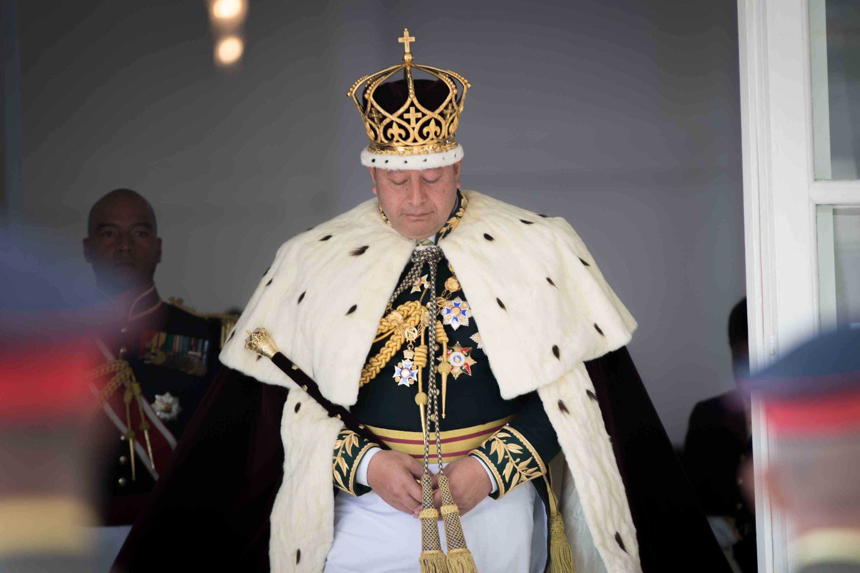 Tongan king Tupou VI wearing regal dress and his crown walks towards the camera during his coronation