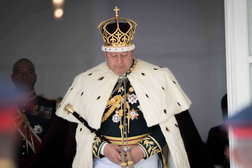 Tongan king Tupou VI wearing regal dress and his crown walks towards the camera during his coronation