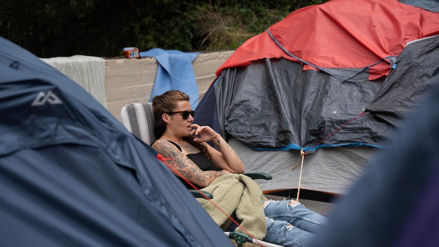 Woman sits on a chair surrounded by tents. 