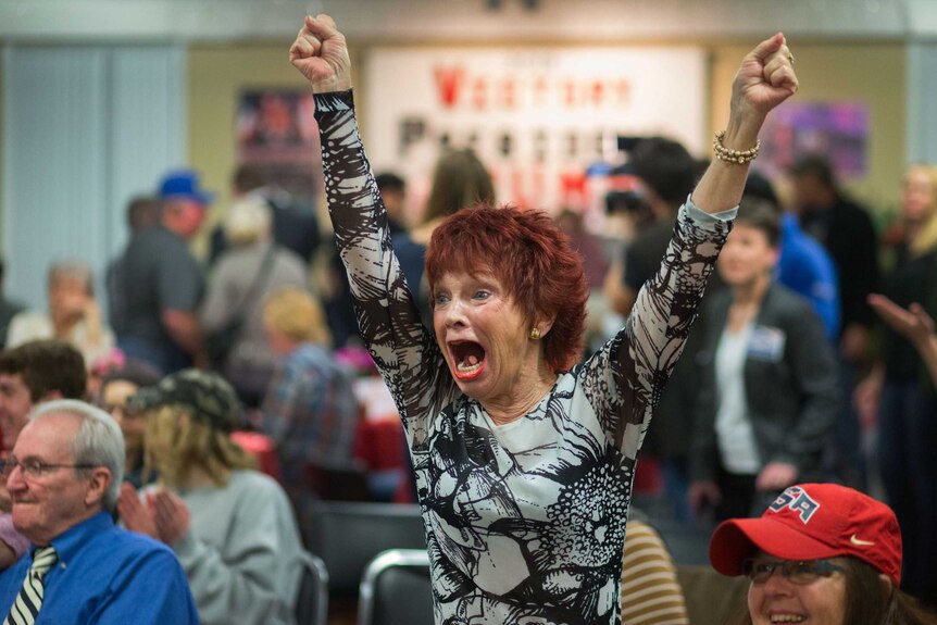 A woman raises her fists in the air triumphantly.