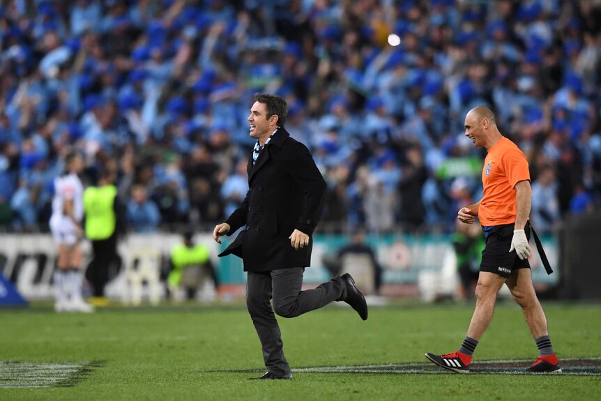 Brad Fittler jogs onto the field in front of a line official as the Blues celebrate an Origin win