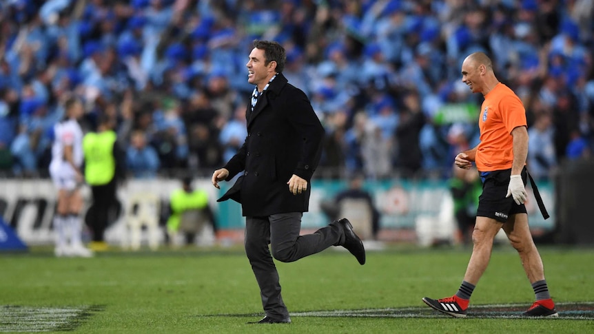 Brad Fittler jogs onto the field in front of a line official as the Blues celebrate an Origin win