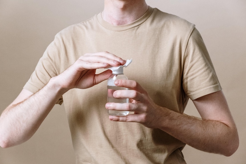 A male torso holding a cotton pad to the top of a bottle of clear liquid.