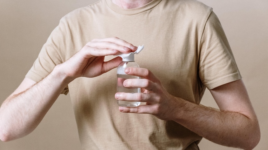 A male torso holding a cotton pad to the top of a bottle of clear liquid.
