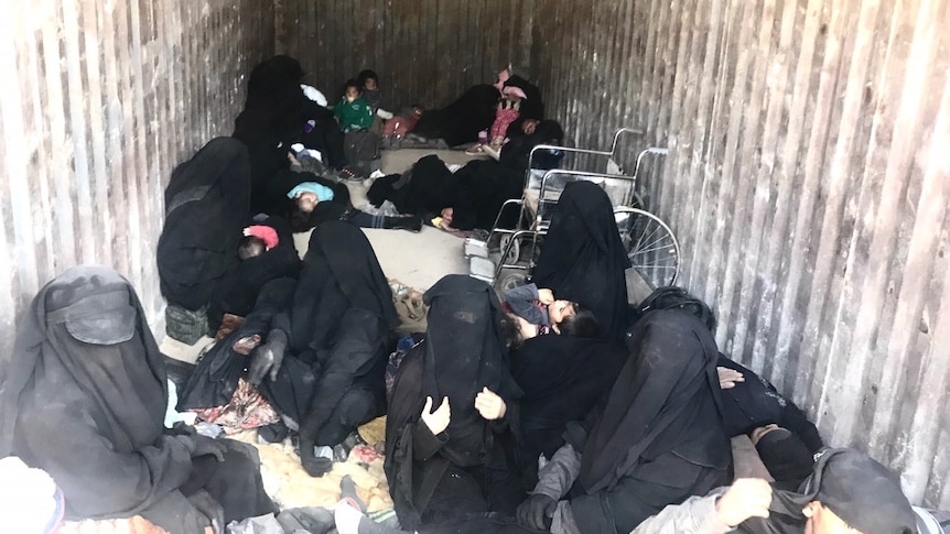 The inside of a truck, with women wearing burquas, most holding small infants and some toddlers.