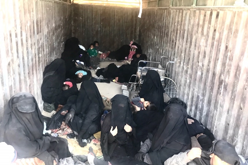 The inside of a truck, with women wearing burquas, most holding small infants and some toddlers.