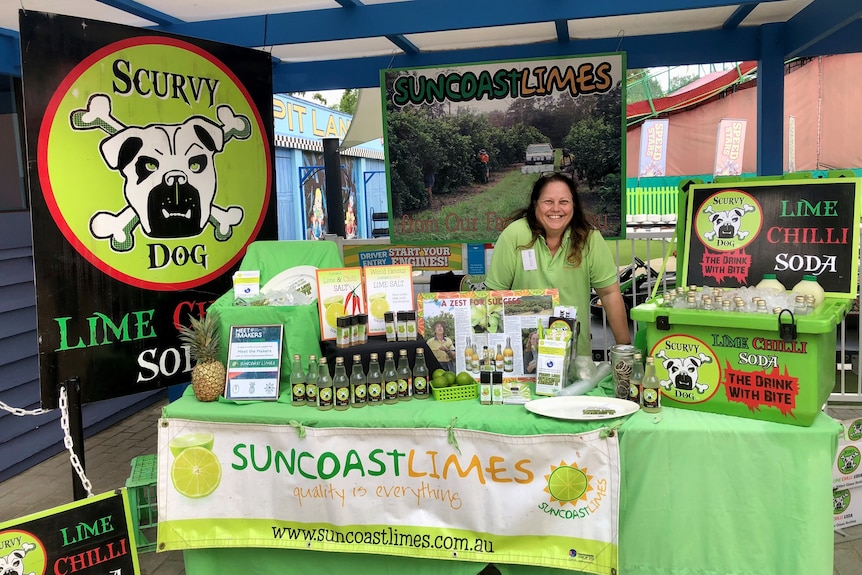 A woman stands at a trade show stand, smiling.