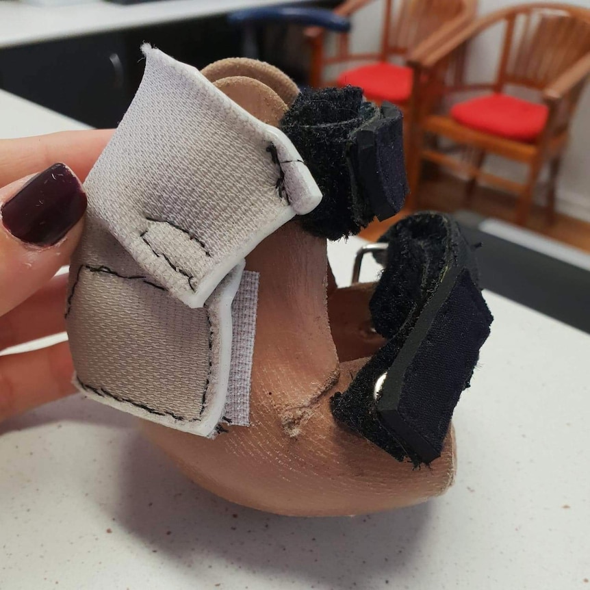 A woman's hand holds a small leather 'bootie' with velcro straps attached to it.