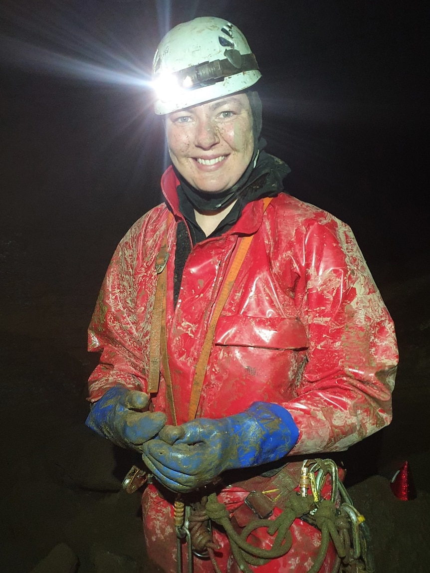 A woman in red overall, white hard hat and a head torch, smiles