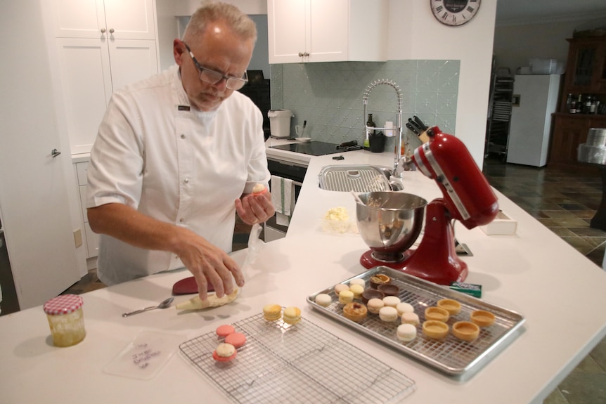 A man in a chef's outfit prepares food for baking in a kitchen.
