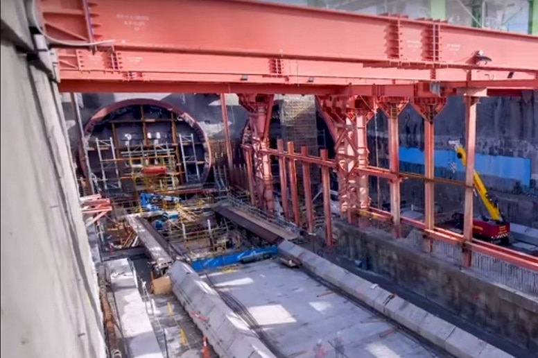 A massive hole in the ground lined with concrete and steel beams with a hole covered with scaffolding at one end.