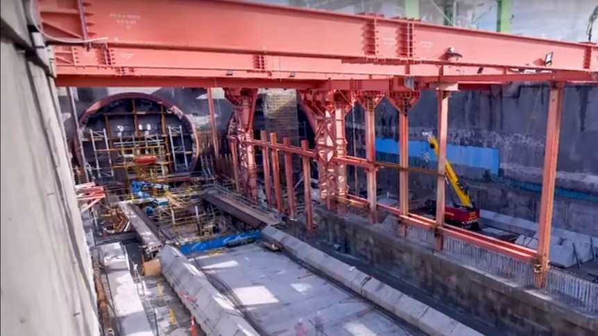 A massive hole in the ground lined with concrete and steel beams with a hole covered with scaffolding at one end.