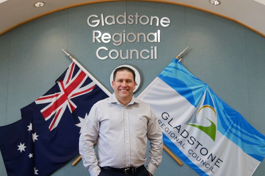 A man with short dark hair stands in front of a Gladstone Regional Council sign in an office.