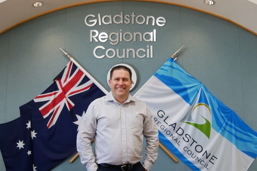 Un hombre con cabello corto y oscuro se encuentra frente a un cartel del Consejo Regional de Gladstone en una oficina.