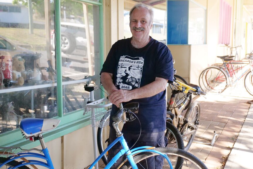 A man in a blue shirt standing in front of a shop and old bikes