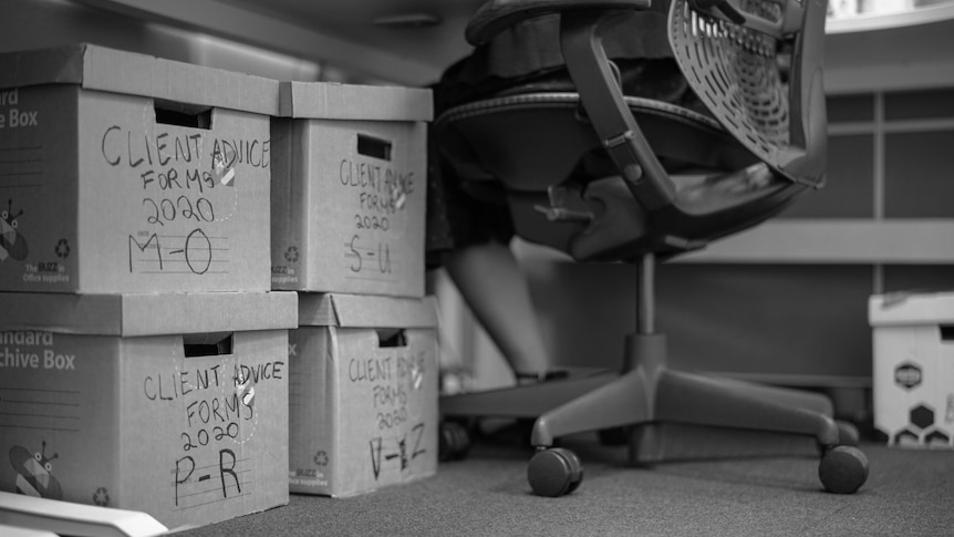 Four stacked boxes under a desk next to a woman in a chair