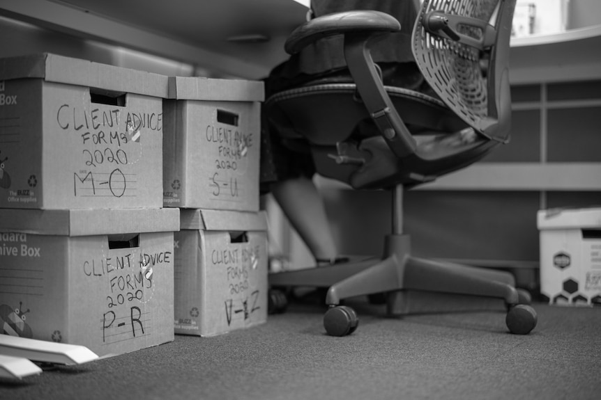 Four stacked boxes under a desk next to a woman in a chair