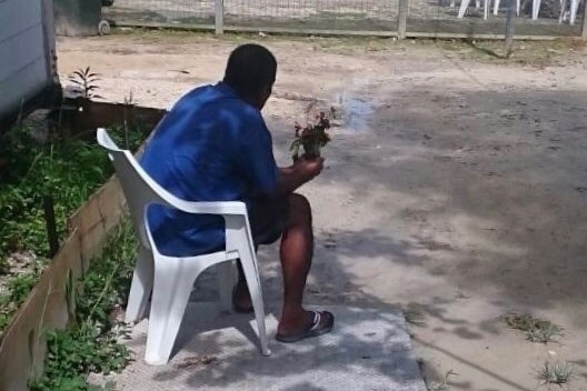 A man sits on a chair holding flowers inside the Manus Island detention centre.