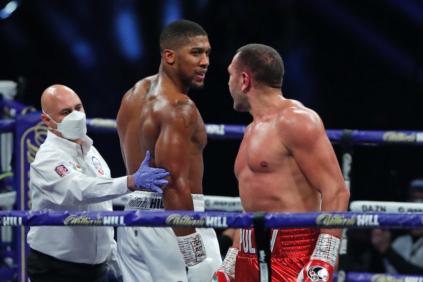 Anthony Joshua and Kubrat Pulev stare at each other with a man in a white shirt between them