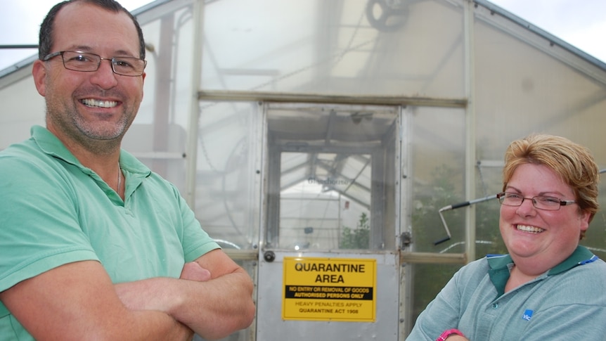 Two researchers standing outside a green house with a quarantine sign