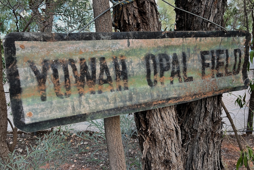 An old rusted sign hanging off a tree that says Yowah Opal Field