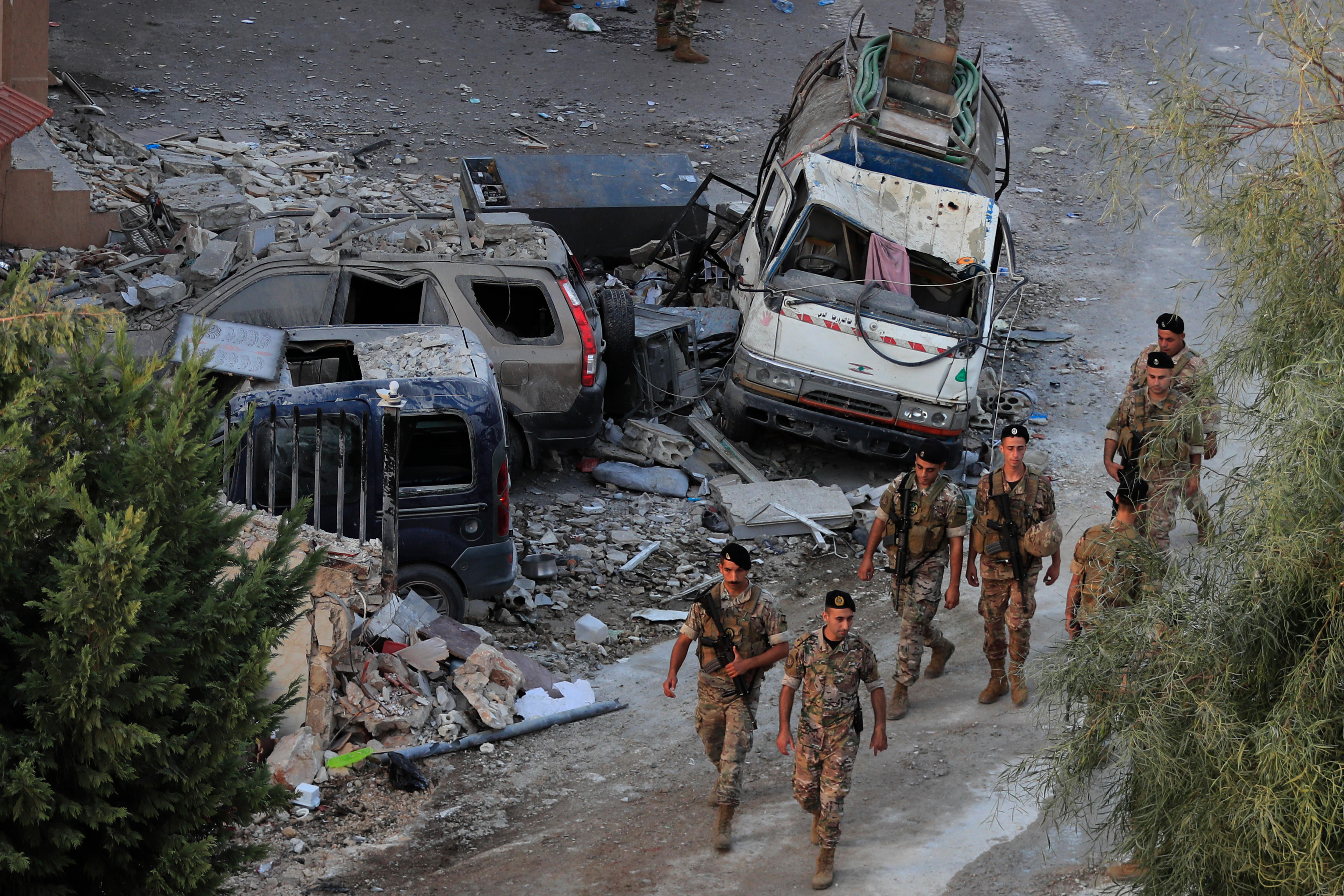 Lebanese soldiers walk in a line past the remains of destroyed cars