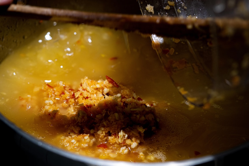 a pot is simmering with oil, chilli, onion and garlic