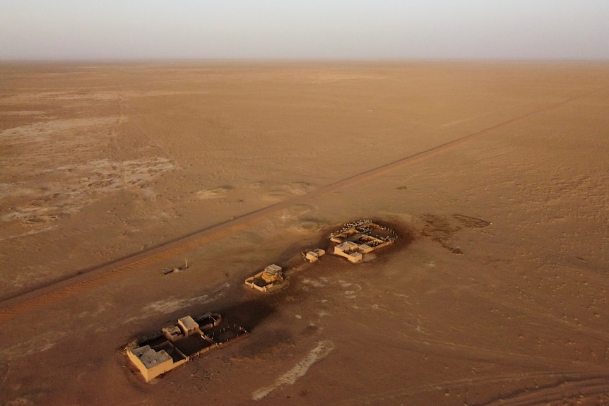 An aerial view of sheep and a pen in a red dusty field in China. 