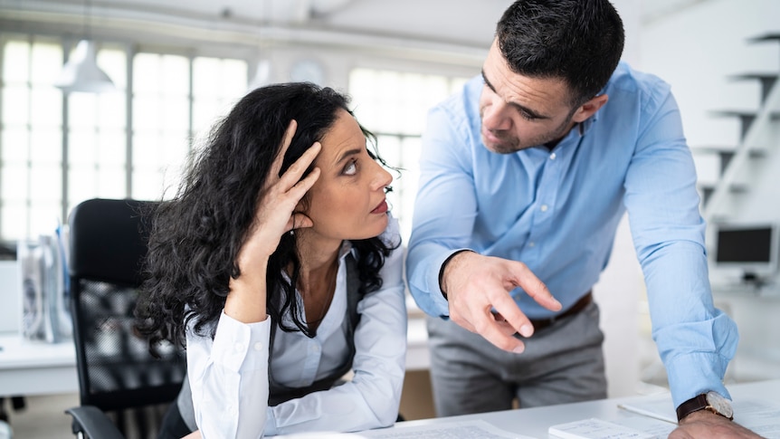 A woman and a man in their thirties at a desk having a deep conversation. Woman looks as though she is losing patience