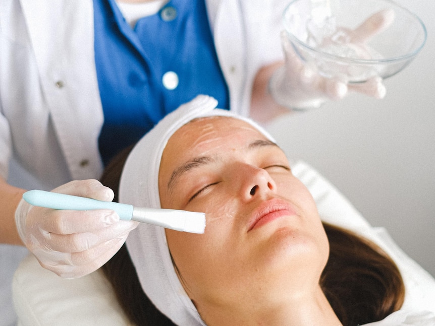 a woman lies on a salon bed as gel is applied to her face